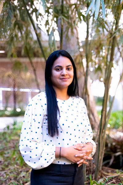 Sneha Kattari smiling outdoors in a white polka dot blouse.