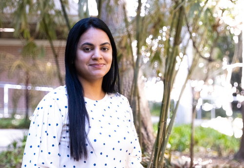 Sneha Kattari smiling outdoors in a white polka dot blouse.