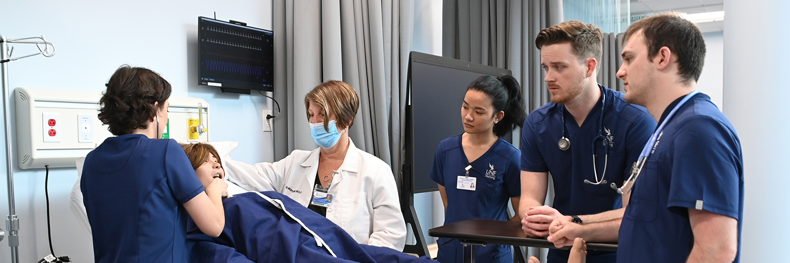 Four students and a professor assisting a patient in a hospital 