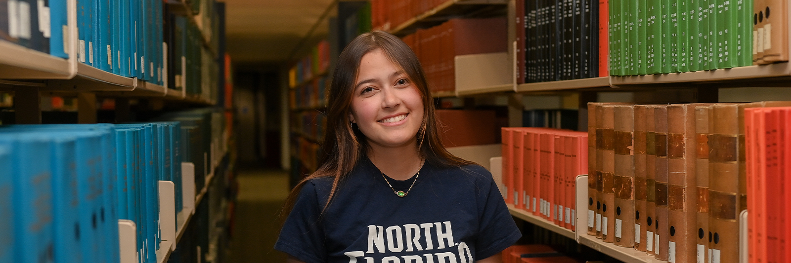 Student smiling standing between library bookshelves 