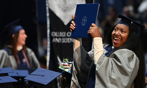 student at graduation holding up diploma