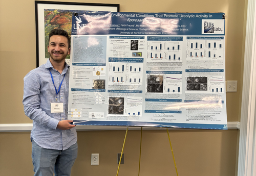 Amar Kosovac standing beside his research poster on environmental conditions that promote ureolytic activity in sponges.