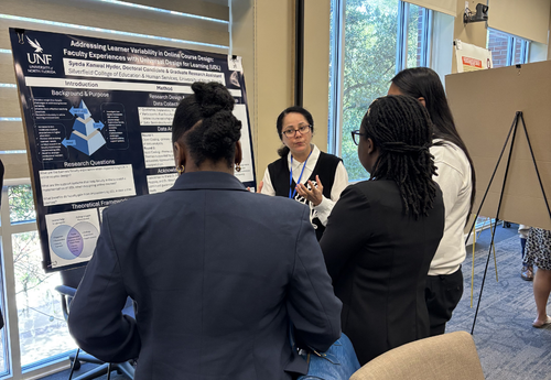Syeda Hyder presenting her research poster on learner variability in online course design to a small group of attendees at an academic event.