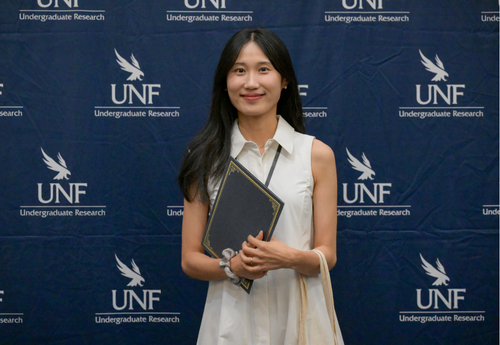 Woman in white button down holding award at UNF Student Research Symposium