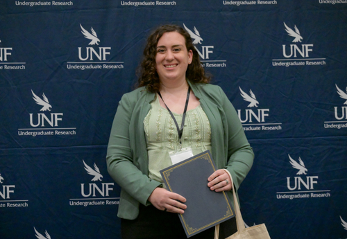 Smiling woman in green with award at UNF Student Research Symposium