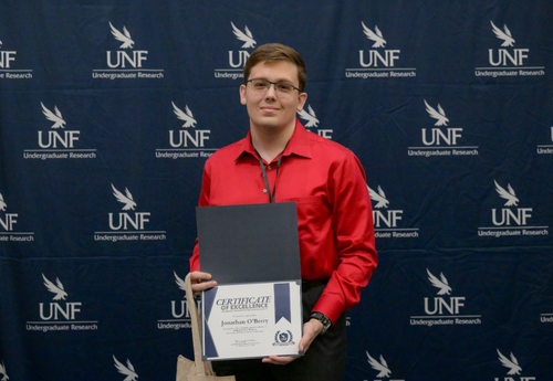 Man in red button down holding Certificate of Excellence at UNF event