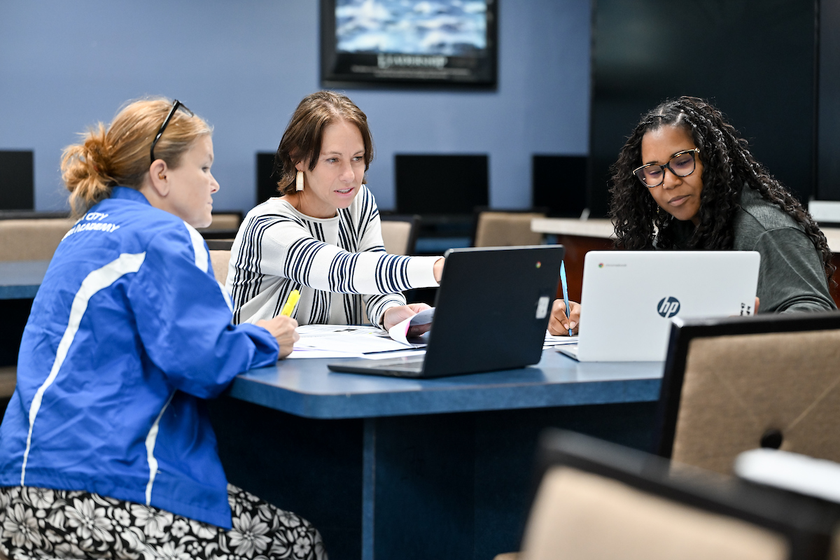 Three women sitting at a table reviewing on two laptops