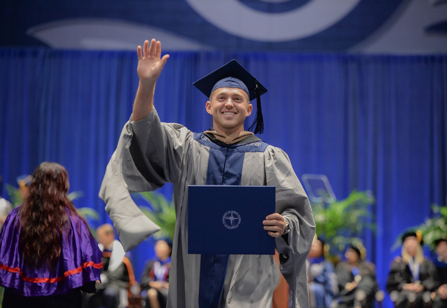 Male grad student waving after receiving his diploma