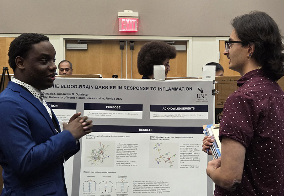UNF student researcher presenting his poster to another student