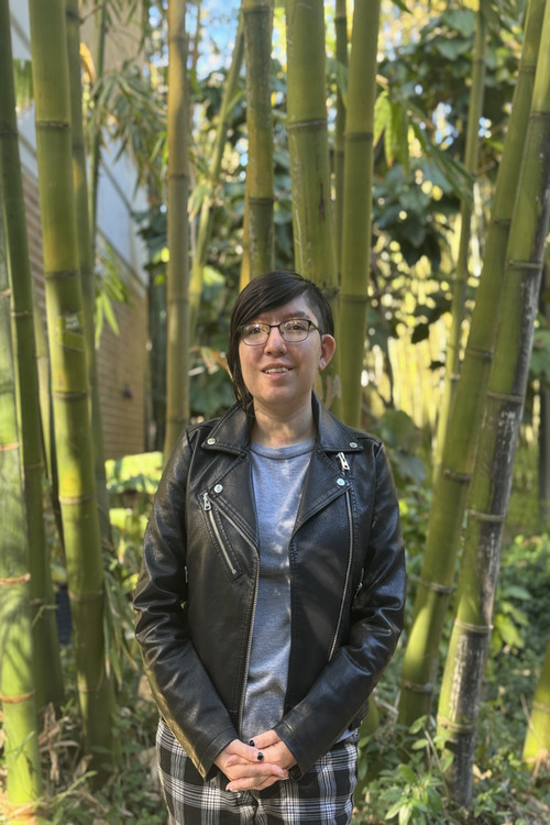 Ziena smiling with her hands together in front of bamboo garden