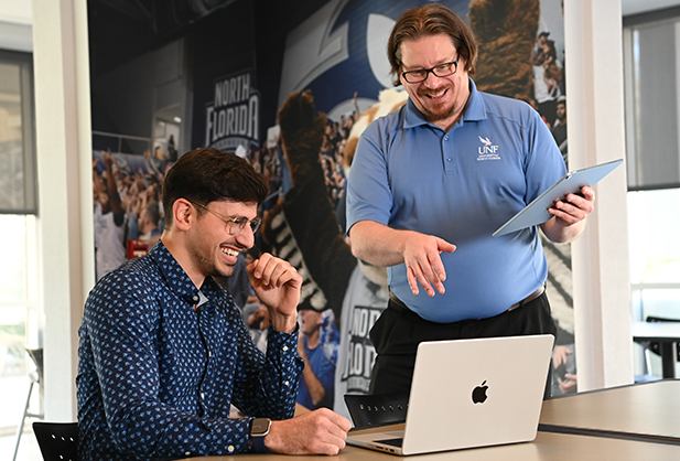 Professor and student looking over a laptop while laughing