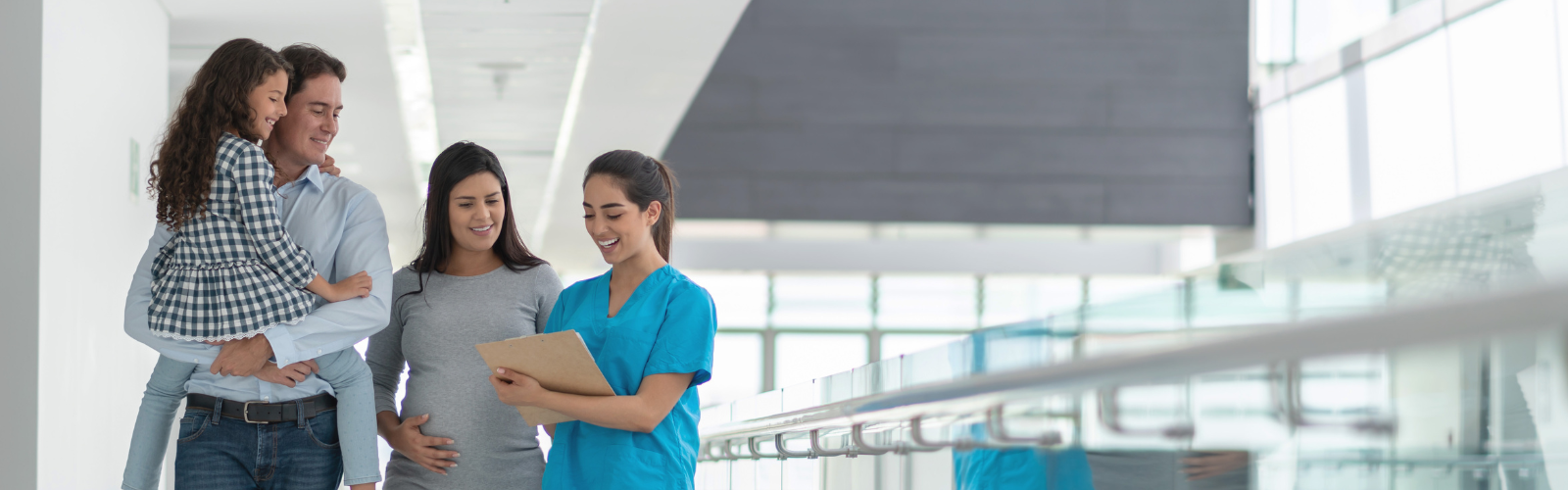 Female nurse with clipboard talking to a pregnany mom and dad is holding his daughter