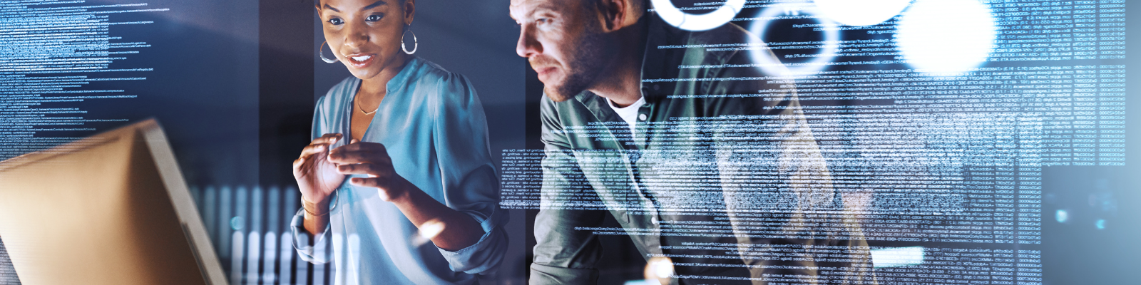 a woman and man standing next to a computer with coding on the screen
