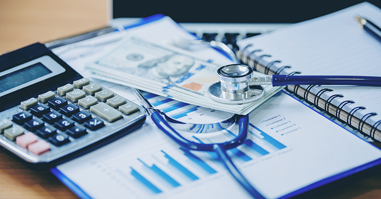 calculator money stethoscope on top of charts and notebook