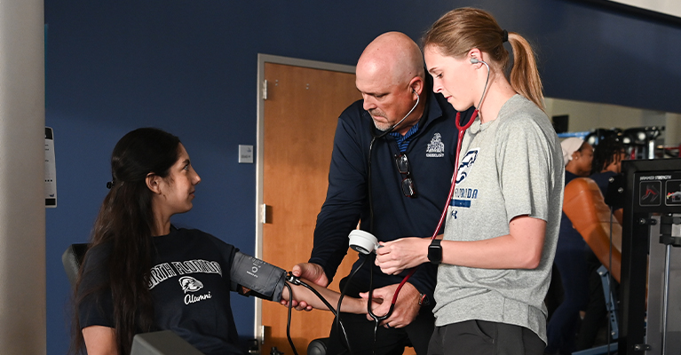 UNF student and professor checking patient's blood pressure in a gym setting