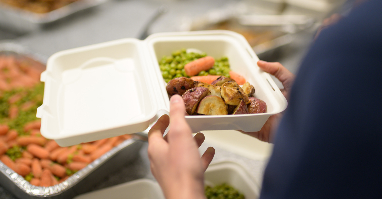 person holding a take-out tray of potatoes peas and carrots