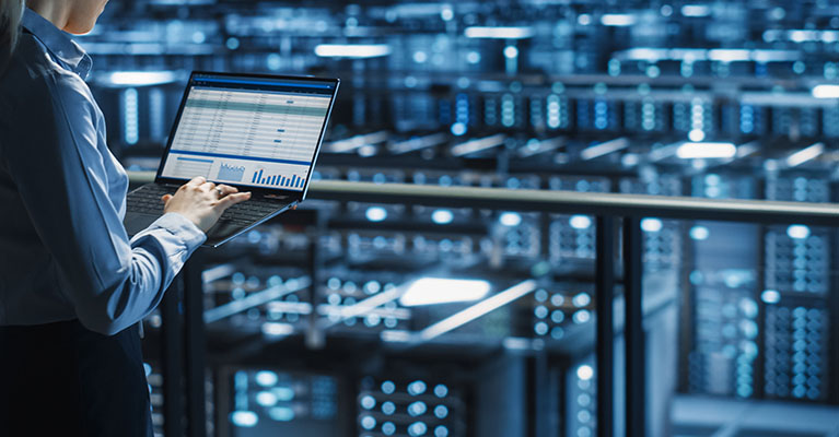 person working on a laptop overlooking a roomful of servers
