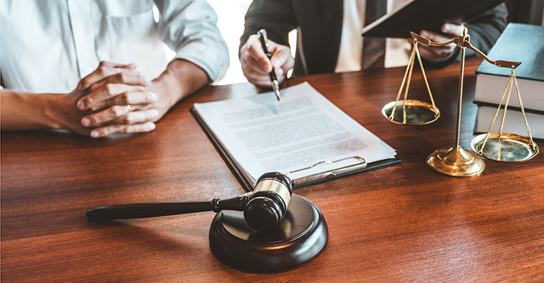 a gavel and scales of justice on a desk with lawyer and client going over a contract