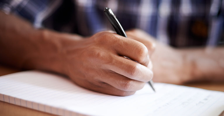 man writing in a notebook with a pen