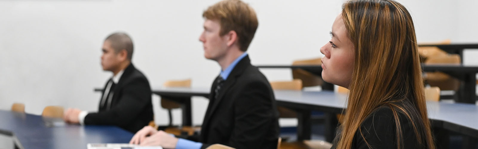 three students listening in a classroom