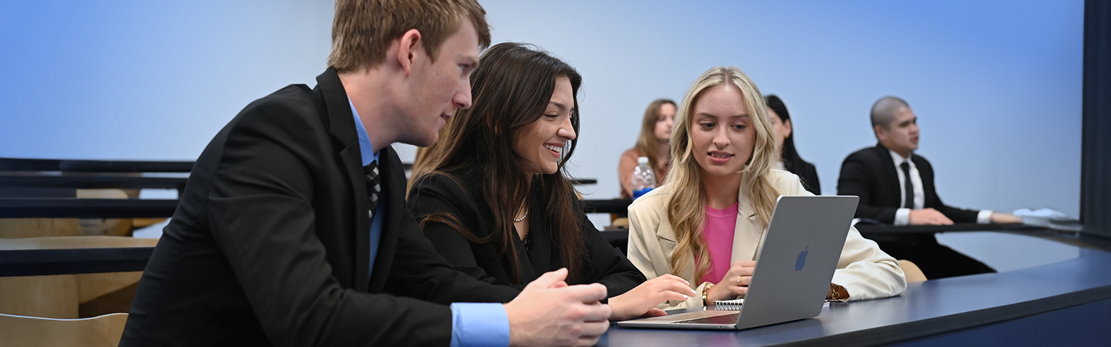 classroom of students with three in focus looking at a tablet