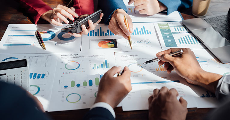 three people pointing at monthly report charts