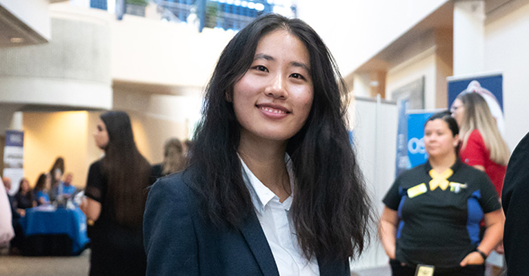 Student smiling in business attire in a conference hall holding a folder