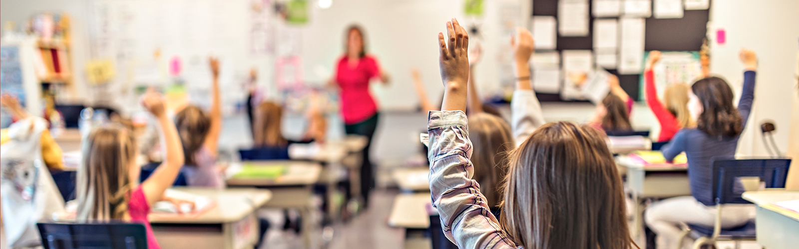 elementary students raising their hands with a teacher in the background