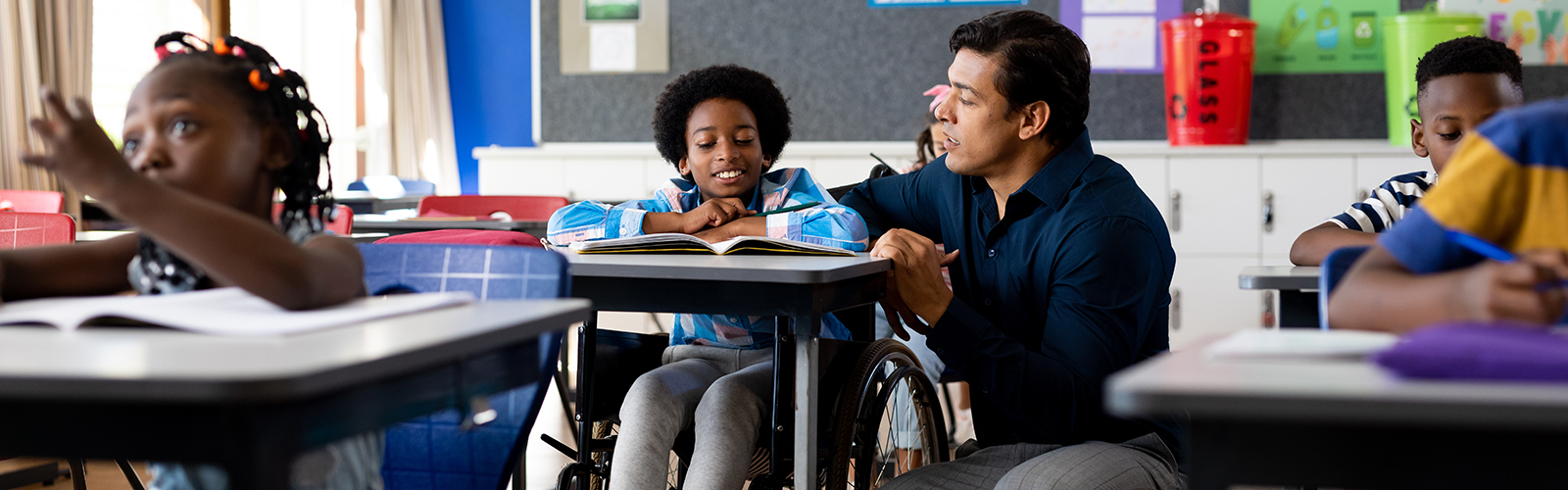 a teacher talking with a boy in a wheelchair at his desk