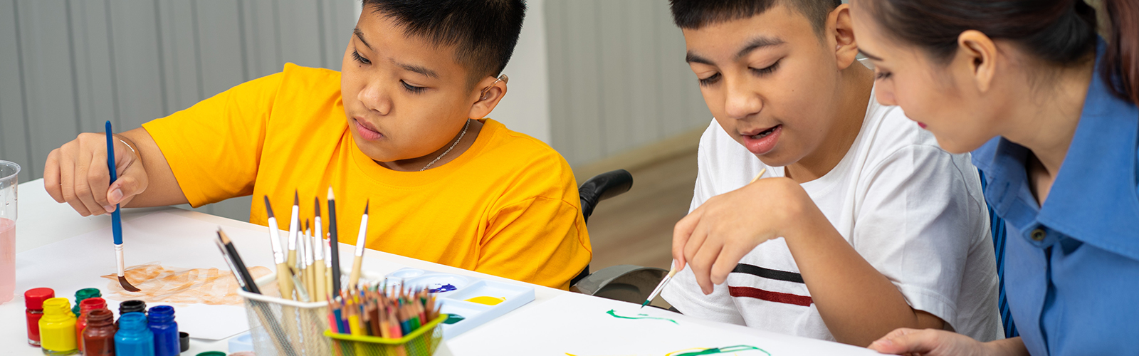 two students painting with their teacher