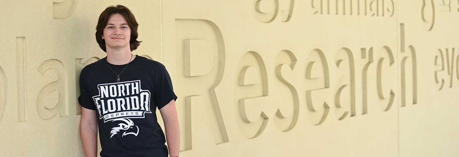 student leaning a wall with the word research engraved in it