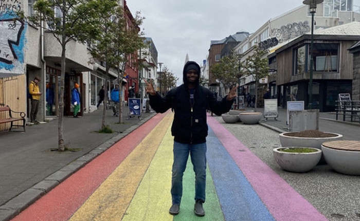 Akintoye Oyedola standing on a rainbow street making a double peace sign with his fingers.