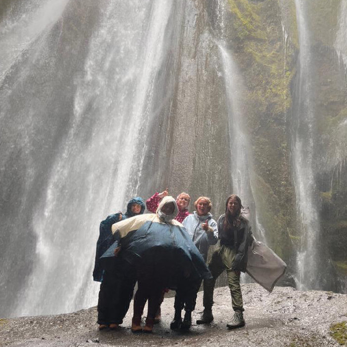 Students in rain jackets standing below a waterfall in Iceland