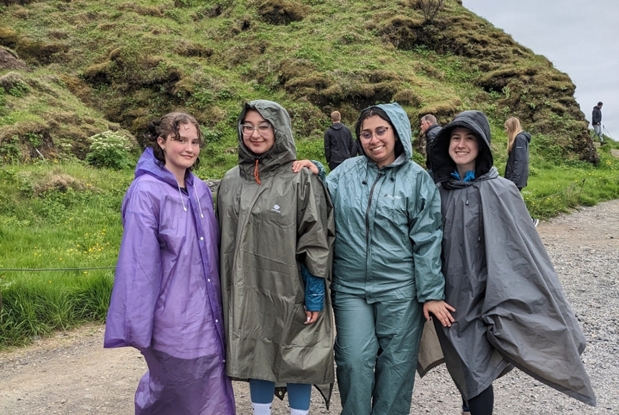 Students in rain ponchos pose on a green hill