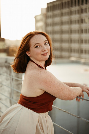 Portrait photo of a woman in an orange halter top posing in front of a river.