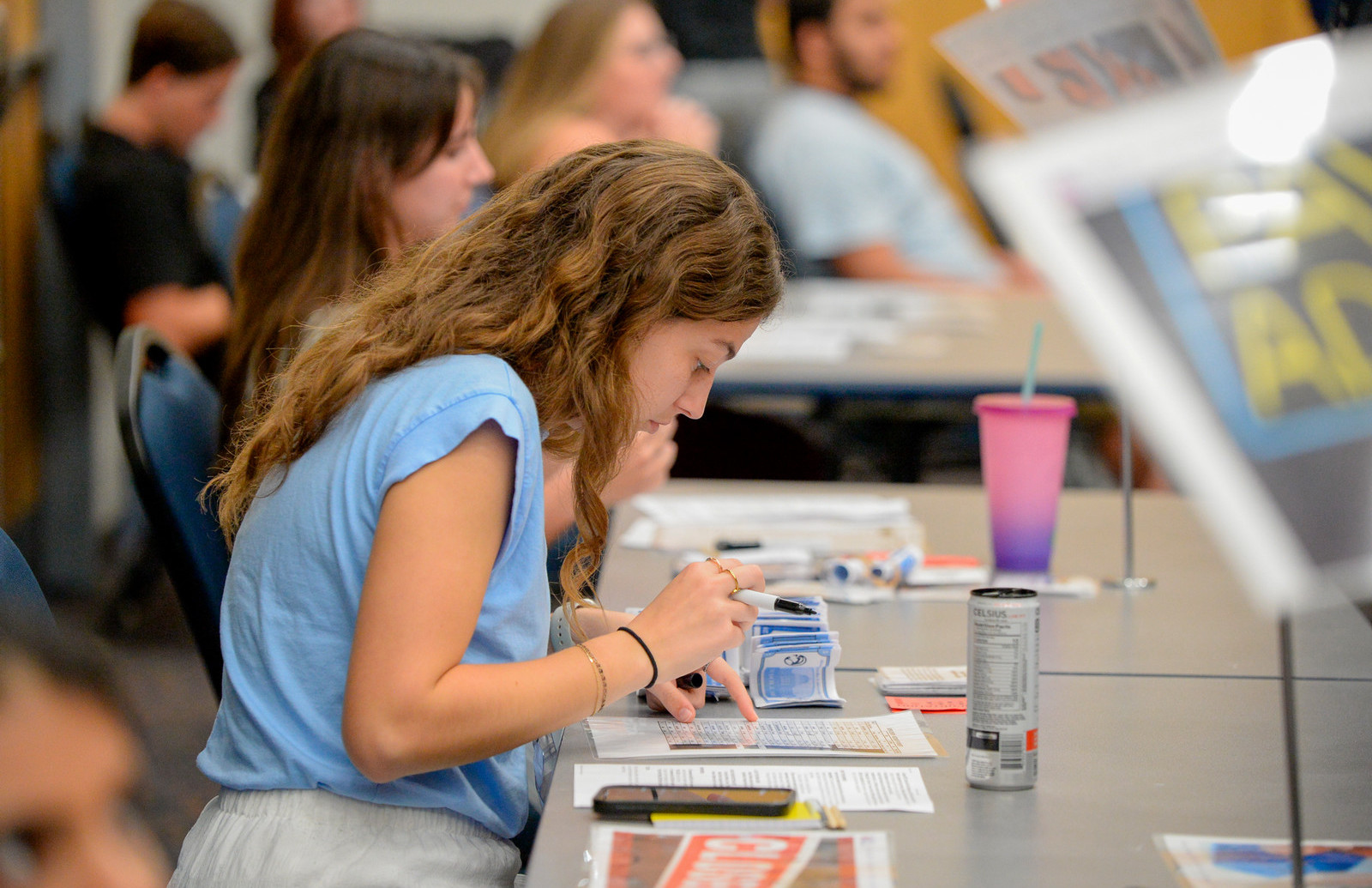 Profile shot of a girl sitting at a table holding a pen and looking at a piece of paper. 