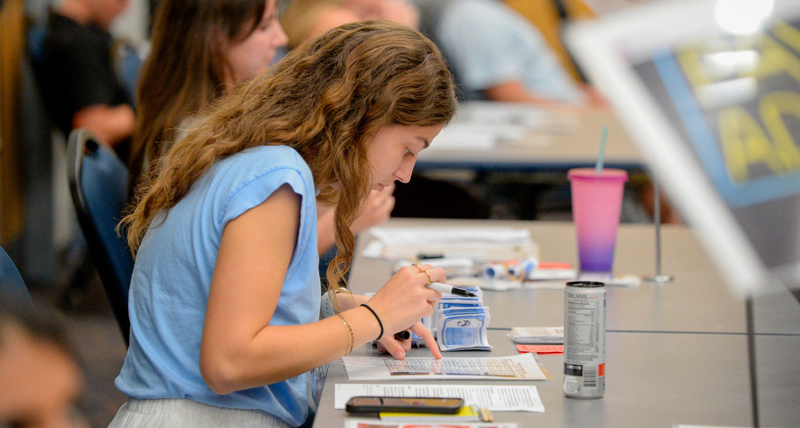 Profile shot of a girl sitting at a table holding a pen and looking at a piece of paper. 