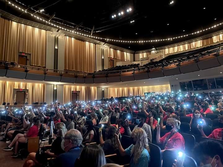 Students in the theater holding phone flashlights