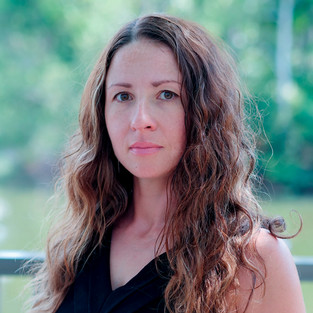 Headshot of woman with brown hair with blurred nature background.