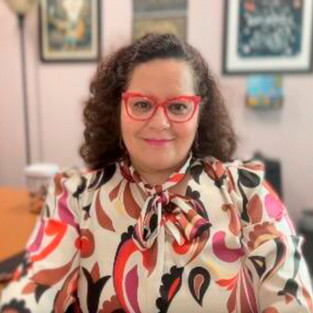 Headshot of woman with curly brown hair and red glasses.