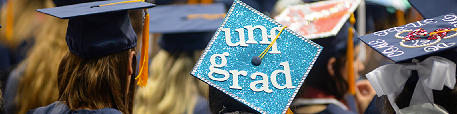 UNF graduates wearing decorated caps and gowns with text of UNF Grad