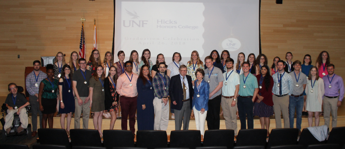 Ann and David Hicks standing with graduating Honors students in an auditorium