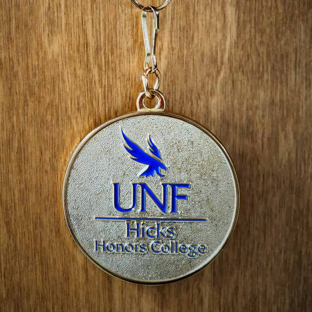 Blue and gold Hicks Honors College medallion with a wood background. 