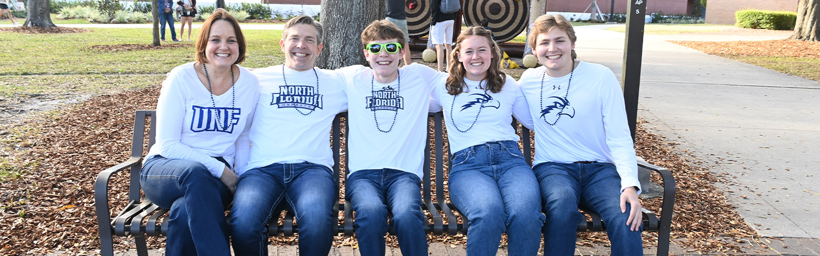A family sitting on a bench at UNF while wearing North Florida t-shirts