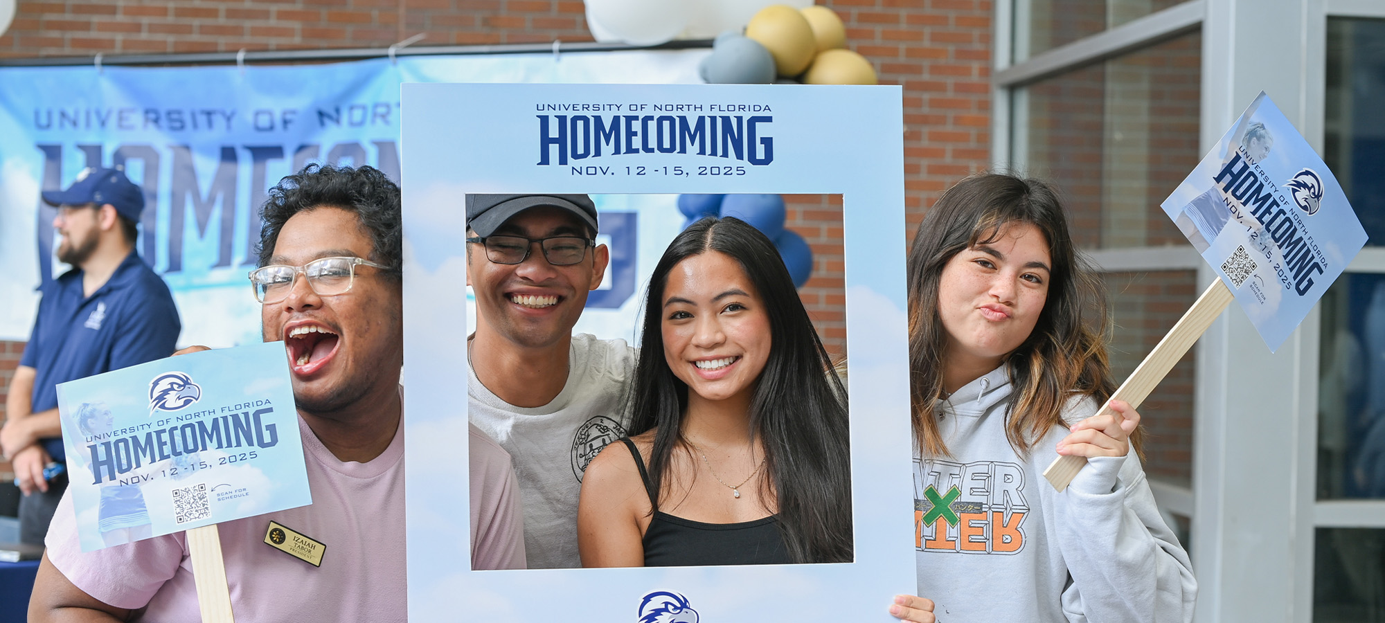 group of students holding homecoming frame and signs in front of a big UNF Homecoming banner