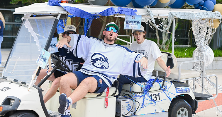 UNF students on a homecoming themed golf cart while wearing hockey jerseys