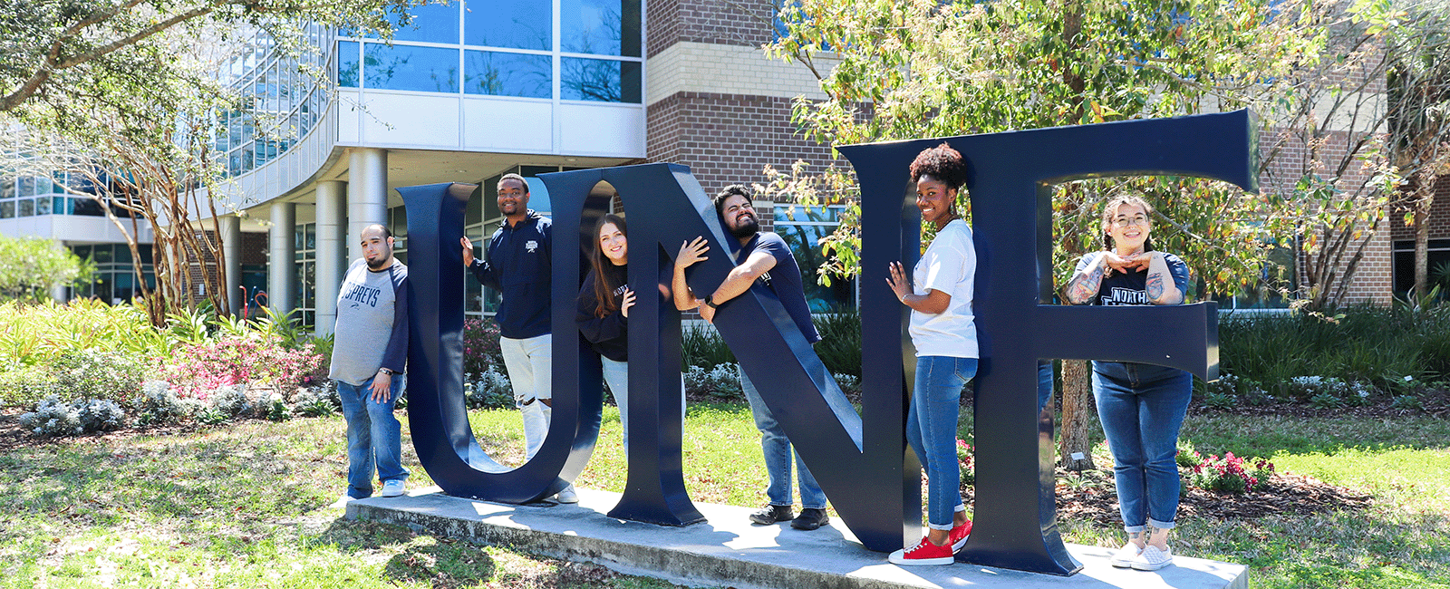 Residence Life Coordinators at the UNF letters smiling and hugging the letters
