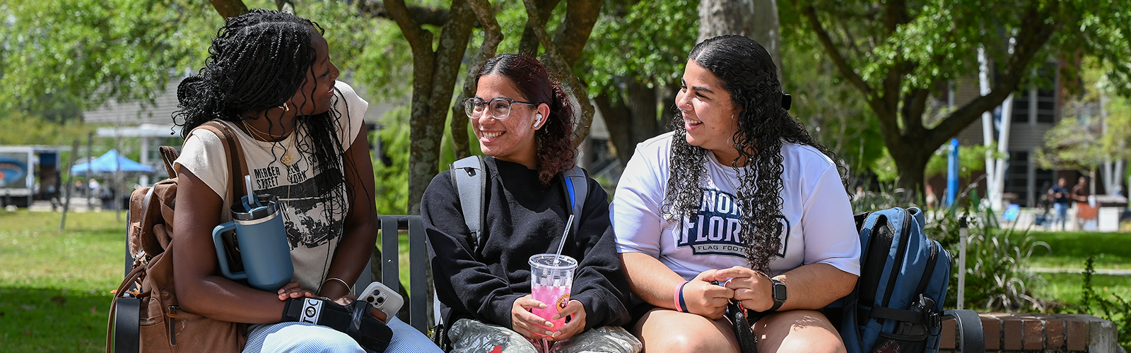 three UNF students on a bench on UNF campus talking and smiling