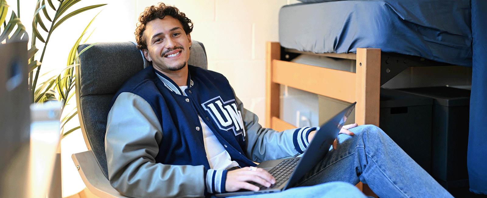 UNF resident smiling on laptop in their UNF themed room on campus