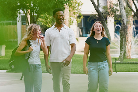 three students smiling and laughing while on UNF campus on a beautiful day